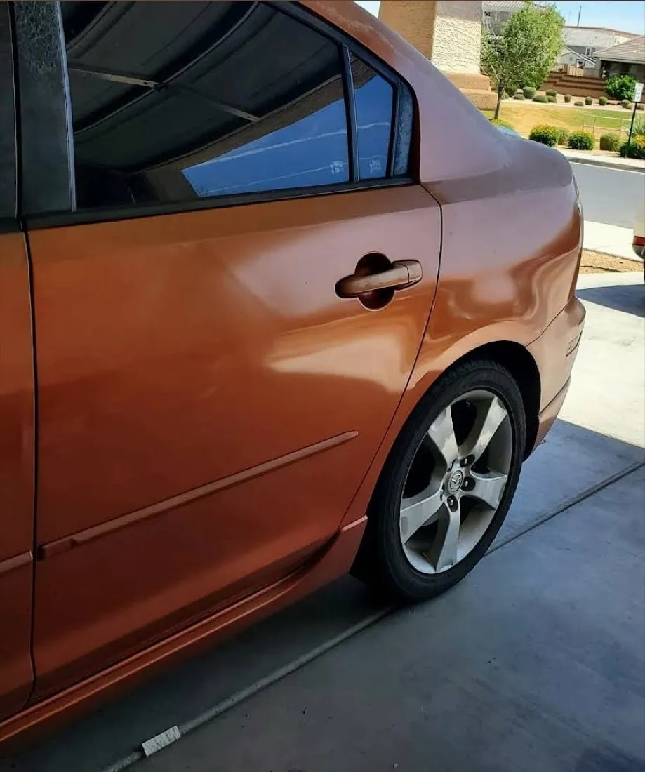 Large door dent on an orange sedan removed with paintless dent repair, factory finish preserved in Apache Junction, AZ, after