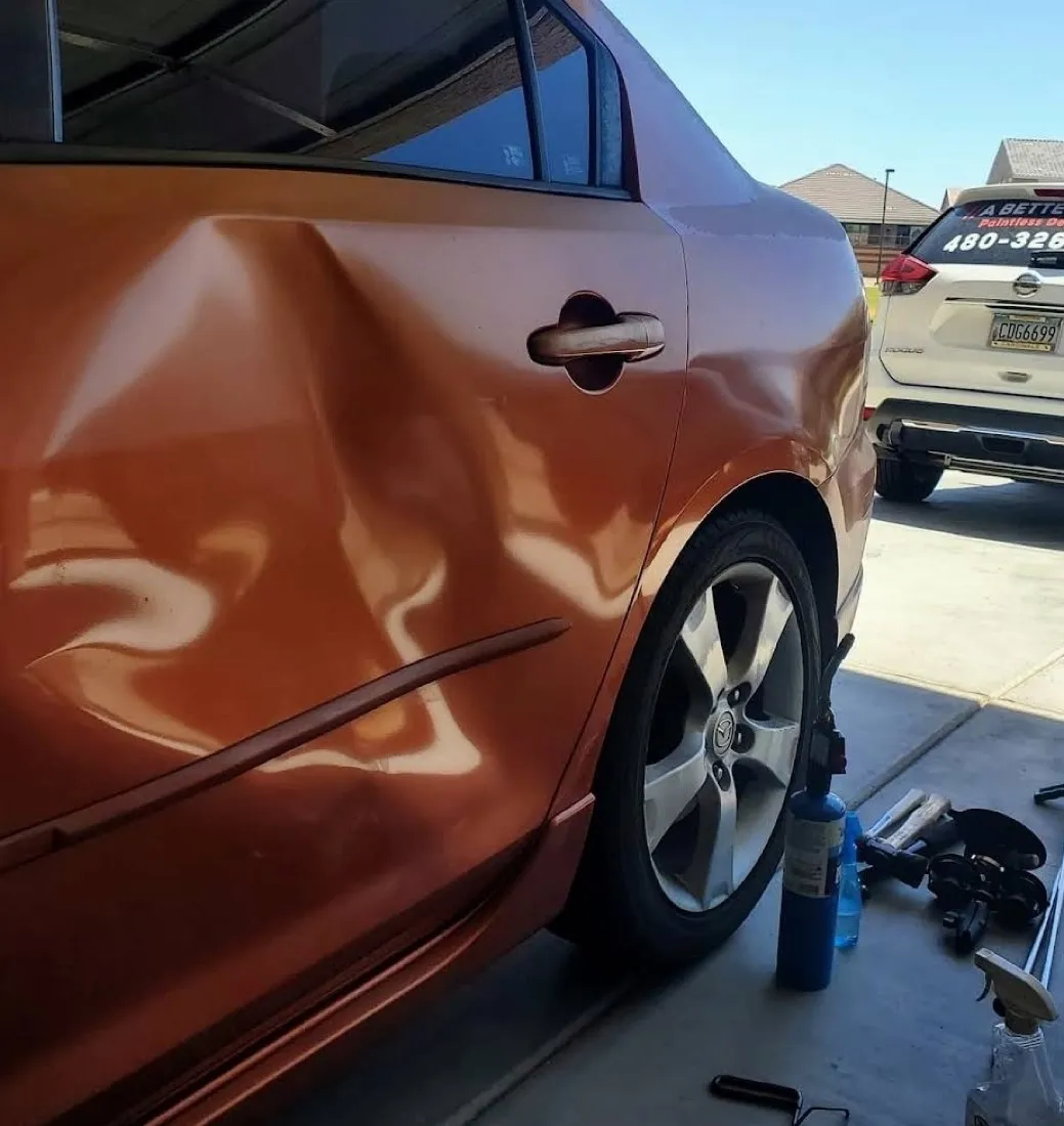 Large door dent on an orange sedan removed with paintless dent repair, factory finish preserved in Apache Junction, AZ, before